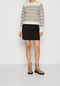 Maglione crema con un motivo geometrico, mini gonna nera con due bottoni frontali e ankle boots beige con suola nera.