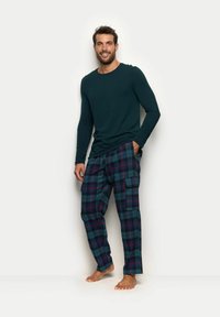 Dunkelgrünes Langarmshirt, kombiniert mit karierter Schlafanzughose in Blau, Grün und Lila. Die Hose verfügt über Seitentaschen und einen lockeren Schnitt.