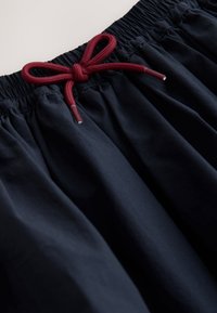 Black fabric shorts with an elastic waist. Features a red drawstring tied in a bow, with a smooth texture and gathered design.
