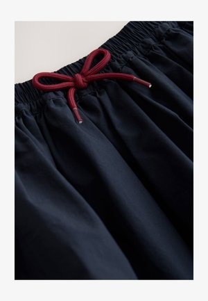 Schwarze Stoffshorts mit elastischem Bund. Sie verfügen über einen roten Kordelzug, der zu einer Schleife gebunden ist, mit einer glatten Textur und einem gerafften Design.