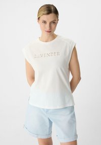 Biała bawełniana koszulka z krótkim rękawem, z napisem "LAVENDER" w jasnoróżowym odcieniu. Koszulka ma luźny krój i delikatny gradient.