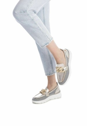 Scarpe slip-on in rete argentata metallica e beige con un accento di corda, caratterizzate da una spessa suola bianca e punta rotonda, abbinate a jeans chiari.