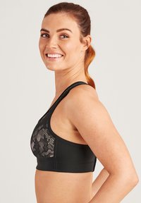 Svart sport-bh med ett nätmönster i blommor framtill, breda axelremmar och en solid strukturera band längst ner. Slät yta överlag.