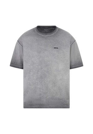 Camiseta gris de manga corta con cuello redondo, textura desgastada y pequeño logo negro "GUESS" en el pecho izquierdo.