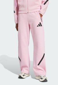 Rosa byxor i mjukt material, med svarta accenter och en Adidas-logga. Löst passande med en rak bendesign och sidofickor.