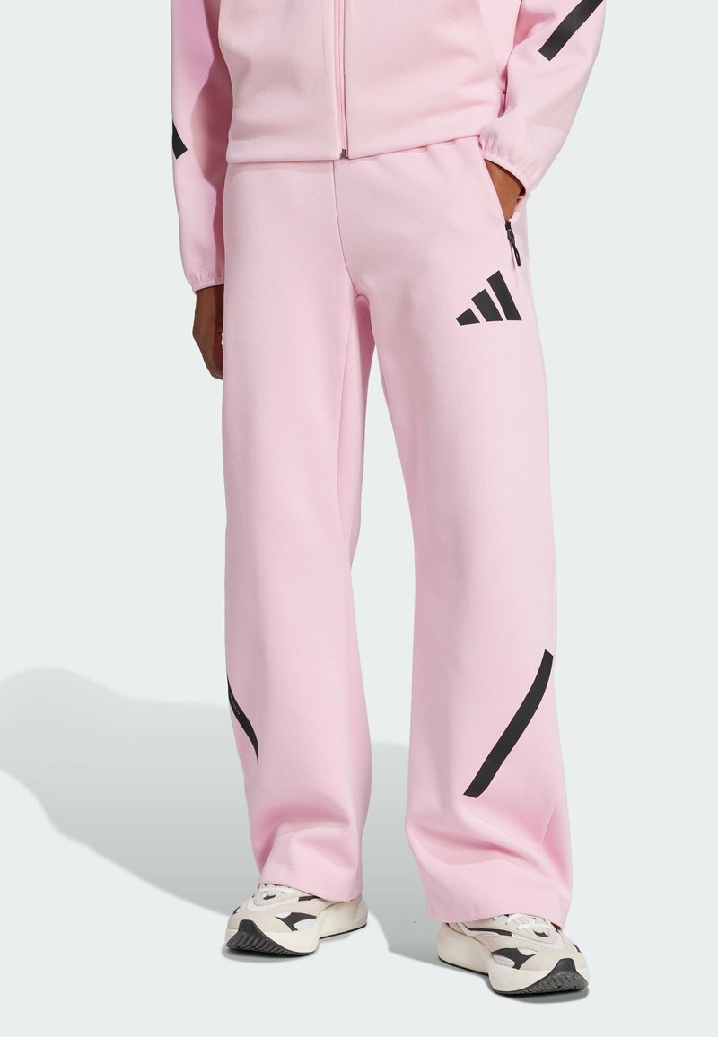 Rosa byxor i mjukt material, med svarta accenter och en Adidas-logga. Löst passande med en rak bendesign och sidofickor.