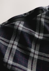 Tissu noir tissé avec un motif à carreaux, comprenant des lignes blanches et bordeaux. Texture douce avec un léger éclat, drapée en plis.