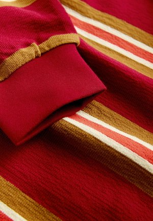 Sweter dziany z bogatymi czerwonymi i złotymi paskami, o teksturowanej tkaninie i prążkowanym detalu z burgundowego koloru na mankietach. Obecne subtelne akcenty w kremowym kolorze.