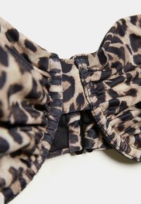 Tissu à imprimé léopard avec coutures élastiques froncées et fermeture à crochet en plastique noir sur un vêtement.