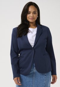 Námořnická blazer s klasickým designem, zapínání na jeden knoflík, dvě přední kapsy a strukturovaná látka, zkombinována s bílou košilí a džínovou sukní.