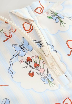 Zipperová textilná vrchná časť s svetlo modrým a krémovým pozadím, zdobená kvetinovými vzormi, vrátane červených jahôd a modrých mašlí, hladk�á štruktúra.