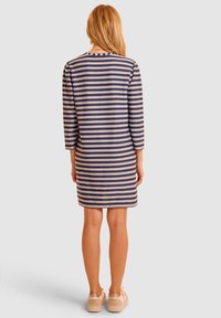 Pasiasta sukienka w kolorze granatowym i beżowym, z rękawami o długości trzech kwart, prostym krojem i miękkim materiałem teksturowanym. Uzupełnieniem stylizacji są codzienne buty.