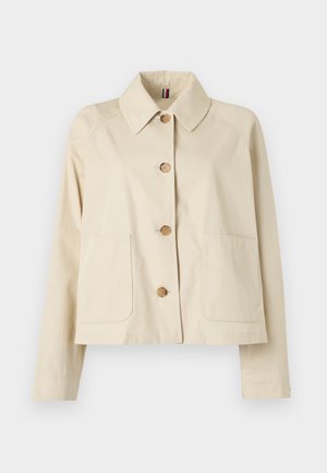 Beige kort jakke med vid krage, fire treskjorter og to frontlommer i et ensfarget bakgrunn.