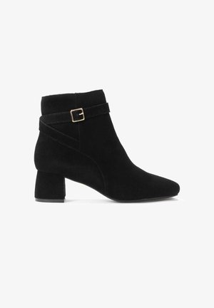 Bottine en daim noir présentant un bout pointu, une finition texturée et une sangle décorative avec une boucle dorée. Talon épais pour plus de stabilité.