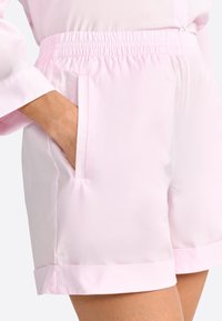 Shorts rose clair en matériau lisse, dotés d'une taille élastique, de poches latérales et d'un ourlet à l'ouverture des jambes.