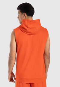Hoodie senza maniche arancione con colletto a cowl, realizzato in tessuto morbido. Presenta una vestibilità rilassata e una texture liscia, adatta per un abbigliamento informale.