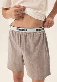 Szare, luźne szorty z białym pasem, na którym znajduje się nazwa marki "HENDERSON" w granatowym kolorze. Materiał wydaje się miękki i przepuszczający powietrze.