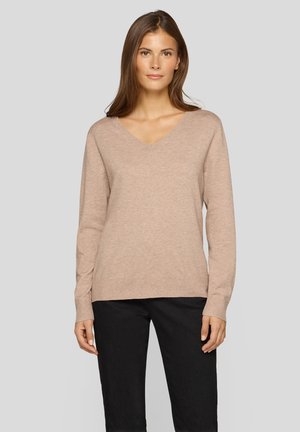 Beiger V-Ausschnitt-Pullover aus weichem, strukturiertem Strick. Mit langen Ärmeln und gerippten Bündchen. Kombiniert mit schwarzer Hose, was das leichte Design hervorhebt.