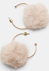 Hoop øreringe med guldtonet metal, der har store, bløde, beige faux fur pom-poner. Designet inkluderer en stud og en rund kugle accent.