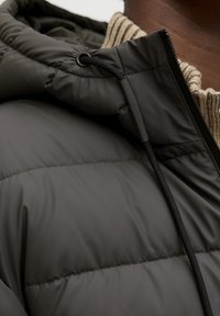 Ciemnozielona kurtka puchowa o miękkiej, gładkiej fakturze. Posiada żebrowany kołnierz oraz regulowany sznurek w kapturze dla lepszego dopasowania.