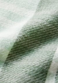Tissu en laine tissé dans des tons de vert clair, avec une texture lisse et un motif à carreaux diagonal, présentant des variations de couleur subtiles et une certaine profondeur.