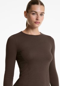Barna, hosszú ujjú, bordás anyagból készült felső, kerek nyakkivágással és karcsú szabással, finom varrási részletekkel az oldalakon.