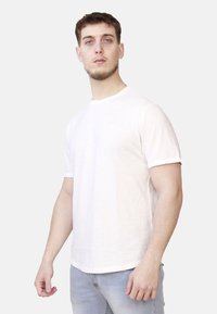 T-shirt bianca in cotone con maniche corte, collo rotondo e un tessuto leggermente texturizzato. Abbinata a jeans in denim blu chiaro.