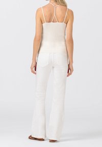 Biała ribbed top na ramiączkach z cienkimi paskami i krzyżującym się tyłem, w połączeniu z białymi dzwonami i brązowymi sandałami, pokazany od tyłu.