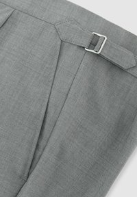 Primo piano di pantaloni in tessuto grigio con una fascia laterale regolabile dotata di fibbia metallica argentata e dettagli di cuciture visibili.