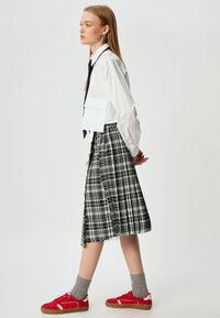Korte witte shirt met een voorzak, zwarte das, geruite grijze rok met rafelige randen, grijze sokken en rode sneakers.