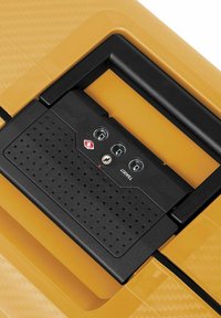 Mango negro texturizado con tres diales metálicos de combinación en una maleta rígida amarilla. Presenta una superficie lisa con acentos en patrones.