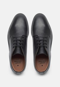 Chaussures en cuir noires avec un bout arrondi, un design à lacets et des coutures contrastantes le long de la semelle et des ouvertures. Texture lisse, accents minimalistes.