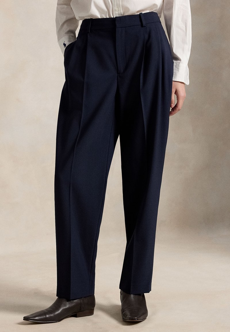 Navy blue wide-leg pleated trousers made of textured fabric, featuring a high waist, side pockets, and subtle creases.
