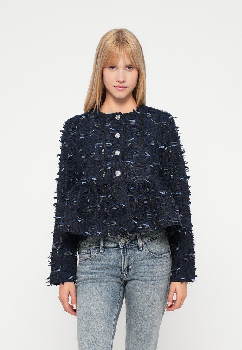 Navy zila īsā jakas izgatavota no teksturēta auduma ar saplēstām detaļām un sudraba pogām. Ar garām piedurknēm un brīvu piegriezumu.