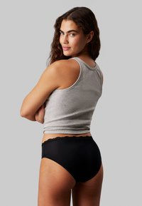 Gray cotton tank top paired with black high-waisted briefs featuring a lace trim. The model is shown from behind, with soft waves in hair.