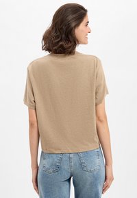 Khaki T-shirt met korte mouwen en een ronde halslijn, zachte textuur en een ontspannen pasvorm, gecombineerd met lichtblauwe hoge taille jeans.