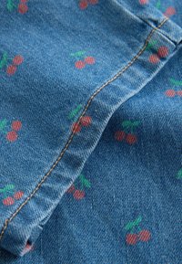 Tela de mezclilla azul con un patrón repetido de cerezas en rojo y verde. Costuras en contraste a lo largo de la costura añaden detalles.