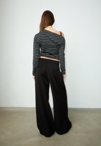 Zwarte wijde broek met hoge taille, gecombineerd met een cropped grijs-zwart gestreept shirt met lange mouwen en een off-shoulder ontwerp.