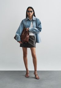 Svetlo modra prevelika jeans jakna, bel rebrast top, črna usnjena mini krilo in rjava usnjena torbica. Črne sandale s trakovi zaokrožijo videz.