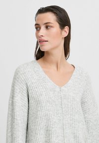 Hellgrauer, gerippter Strickpullover mit V-Ausschnitt, langen Ärmeln und lockerer Passform; weicher Textur und minimalistischem Design.