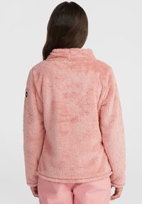Rosa, flauschige Fleecejacke mit hohem Kragen und langen Ärmeln. Besitzt einen abgerundeten Saum und ein kleines Logo am linken Ärmel.