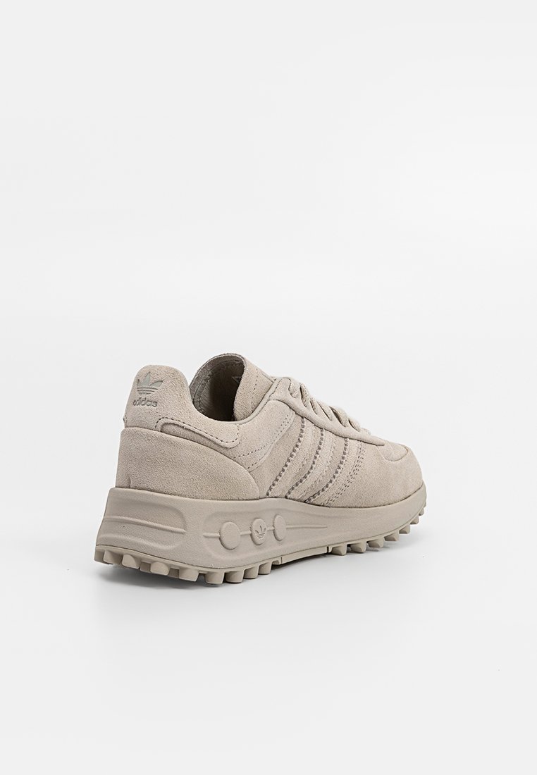 Beige suède sneakers met een laag profiel, voorzien van drie duidelijke zijstrepen, textuuraccenten en een robuuste rubberen buitenzool.