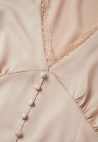 Blouse rose clair avec des boutons recouverts de tissu et une bordure en dentelle le long d'un décolleté en V, affichant un tissu texturé et des détails froncés.