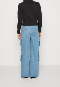 Svart kort hoodie med hög krage, kombinerad med blå vida denim cargobyxor som har sidofickor och en ljus tvätt.