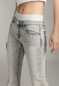 Gray denim jeans with a slim fit, featuring a white waistband labeled "MISS SIXTY," subtle distressing, and contrast stitching.
