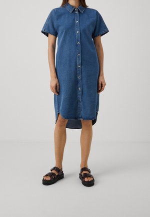 Robe-chemise en jean avec manches courtes, patte de boutonnage, col et fentes latérales. Le tissu est d'un bleu moyen délavé.