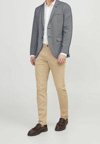 Grau strukturierter Blazer, weißes Hemd, beigefarbene Chinos und dunkelbraune Slipper. Der Blazer hat eine Tasche und einen Ein-Knopf-Verschluss.
