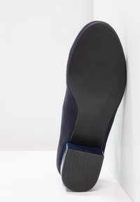 Scarpa in camoscio blu navy con suola in gomma nera testurizzata e accento lucido blu sul tallone. Design leggermente curvo sulla punta.