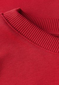 Czerwona tkanina swetra z okrągłym, prążkowanym dekoltem. Gładka tekstura i równe szwy, prezentujące jednolity kolor bez wzorów lub akcentów.