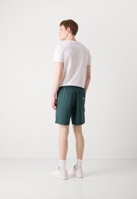 Shorts verts avec ceinture élastique, poche arrière et texture lisse. Associés à un t-shirt blanc uni et des baskets légères.